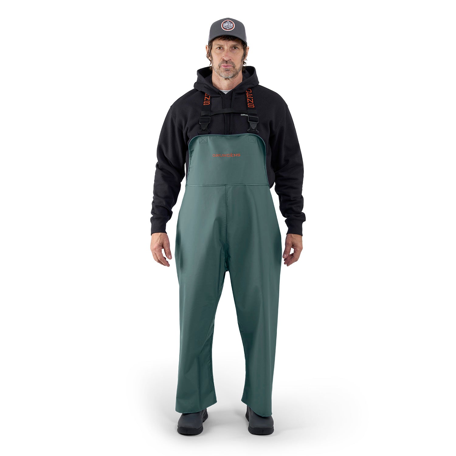 Green waterproof bib overalls worn by a man, paired with a black hoodie and cap.