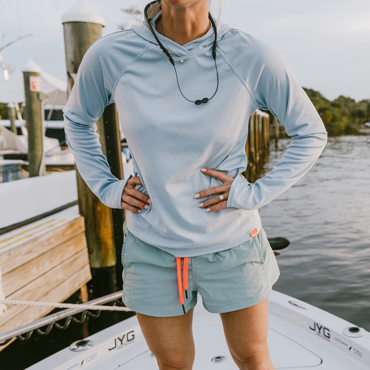 A woman wearing a Zephyr colorway tough sun hoodie, standing on a boat at a marina.