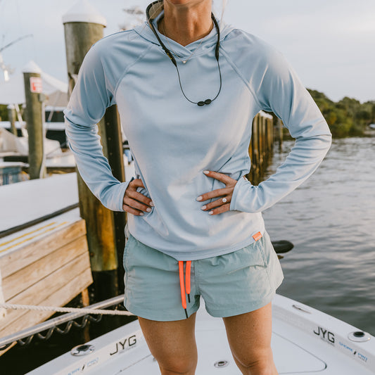 A woman wearing a Zephyr colorway tough sun hoodie, standing on a boat at a marina.